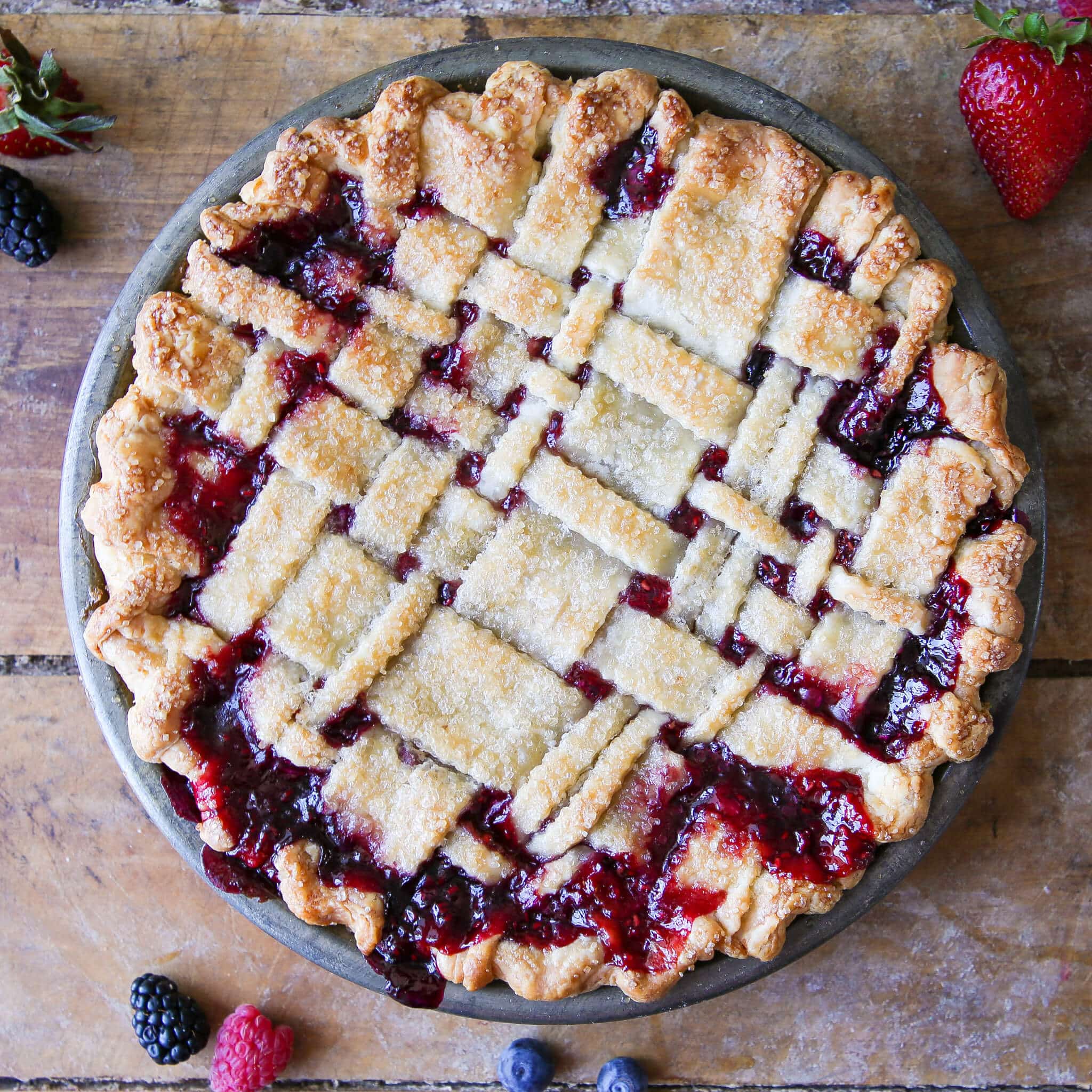Entire mixed berry pie on a wood backdrop in a metal tin.