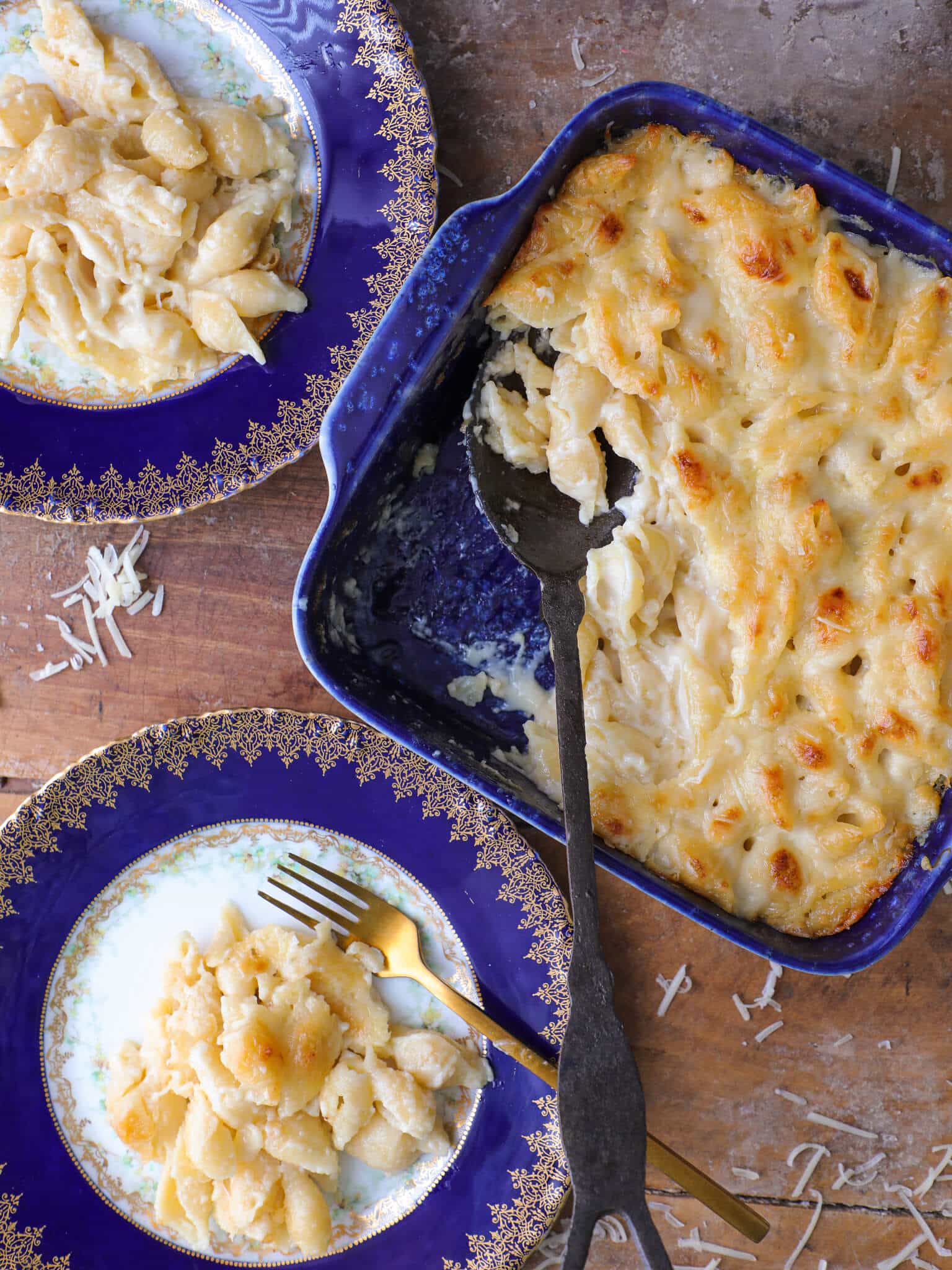 Two plates of white cheddar mac and cheese next to a blue baking dish full of the rest.