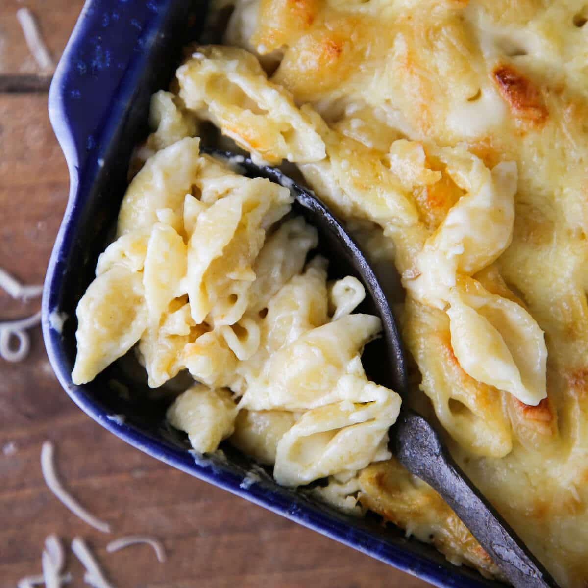 A spoon serving a portion of white cheddar mac and cheese from a blue baking dish.