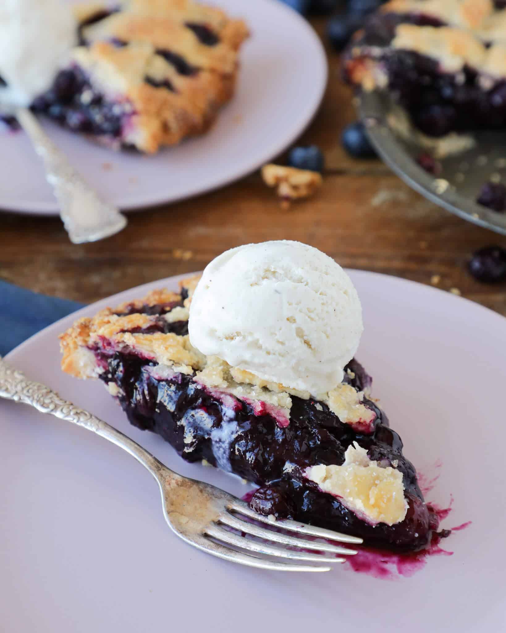 A slice of blueberry pie on a light lavender plate.