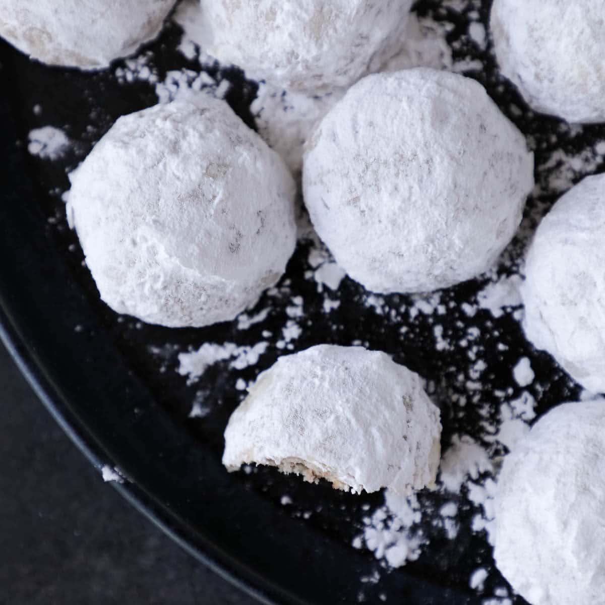 A group of white snowball cookies on a black plate.