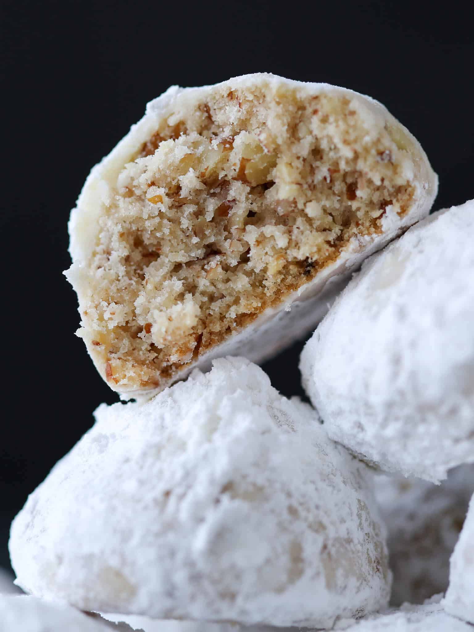 Three snowball cookies with the top one showing a crumbly interior.