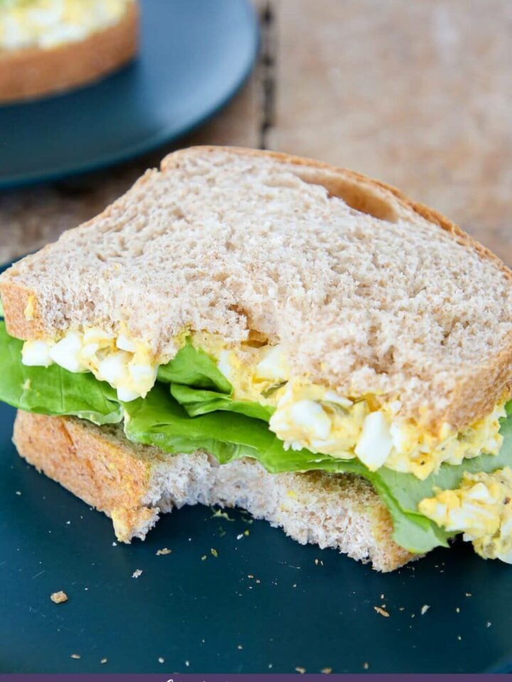 Sliced whole wheat sandwich bread slices piled with deviled egg and green lettuce to make a sandwich.