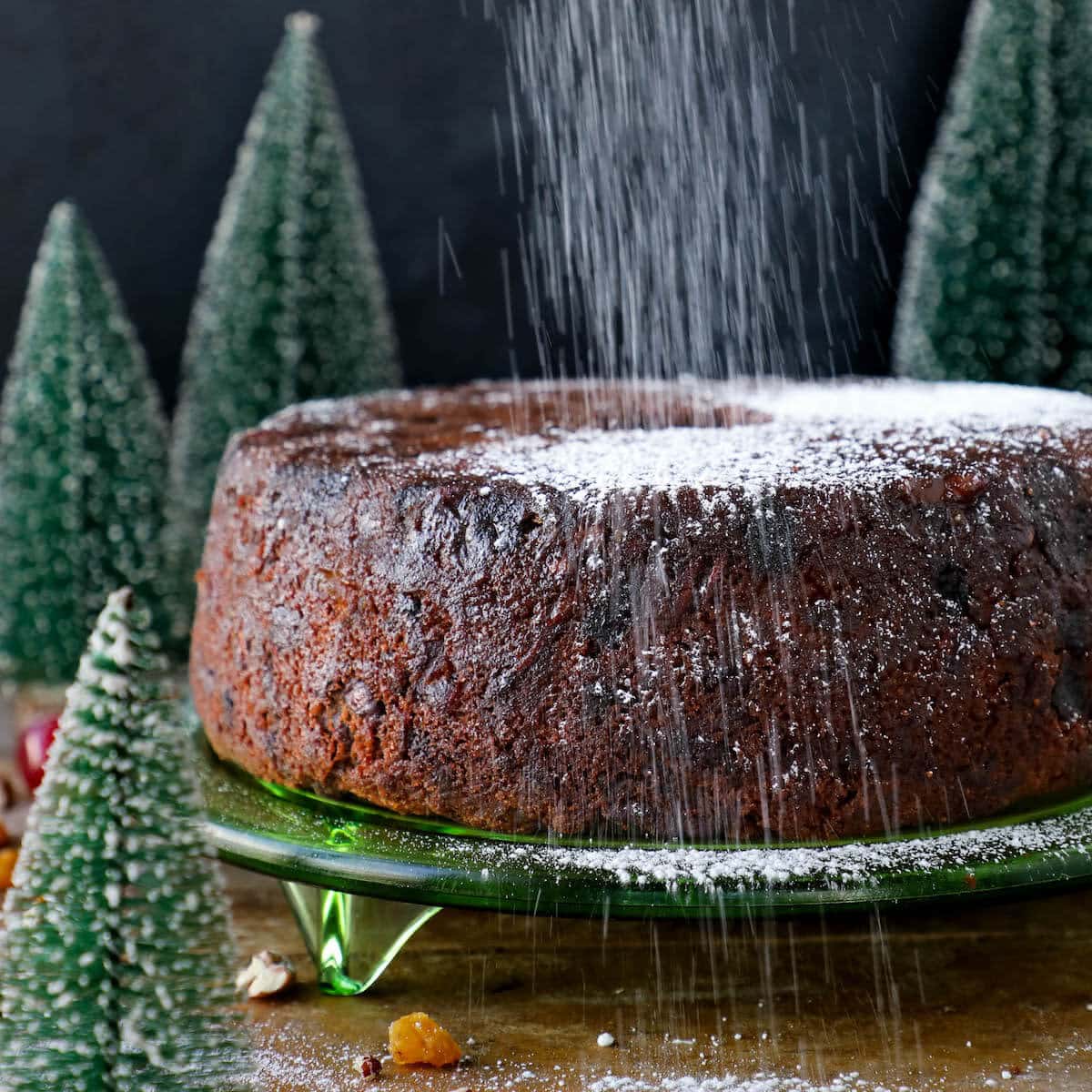 fruit cake unsliced being dusted with confectioners sugar.