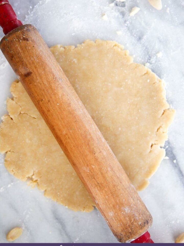 An almond flour pie crust on marble surface with rolling pin.
