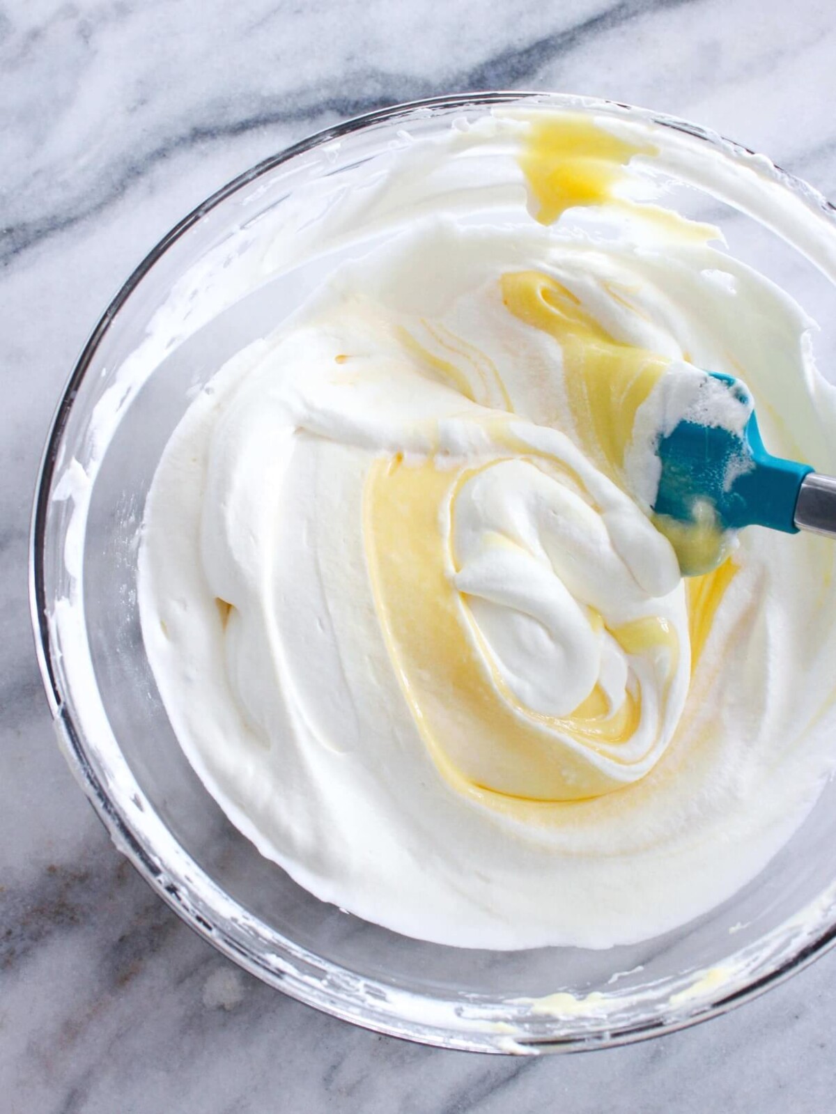 Lemon Curd Whipped Cream being folded in clear bowl on Marble Slate.
