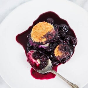 blueberry cobbler on white plate with vintage spoon.