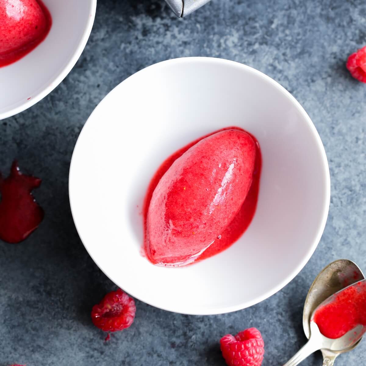 Raspberry sorbet serving in a white bowl on a dark marble background.