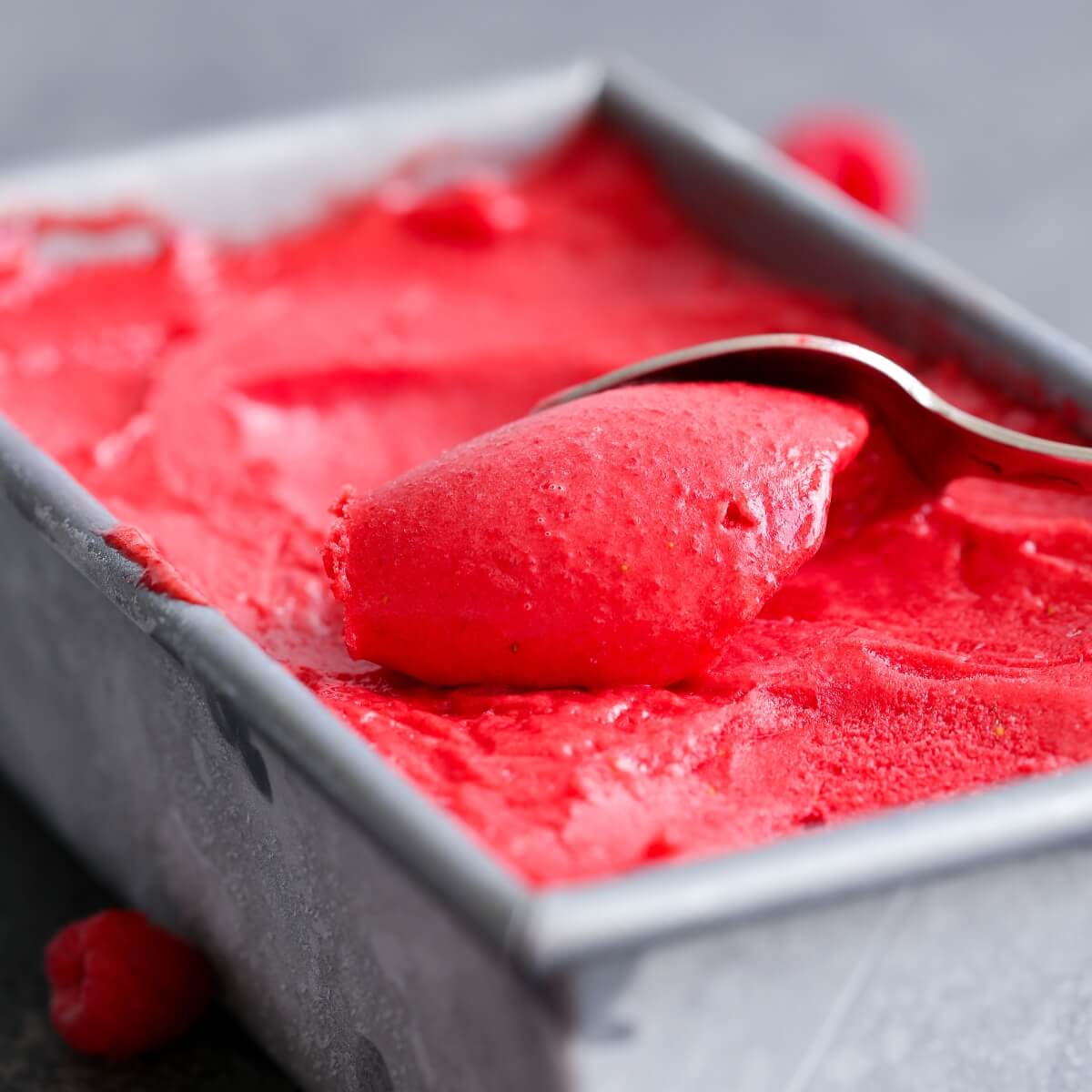 Raspberry sorbet in a metal cannister with a spoon curling a serving off of the top.