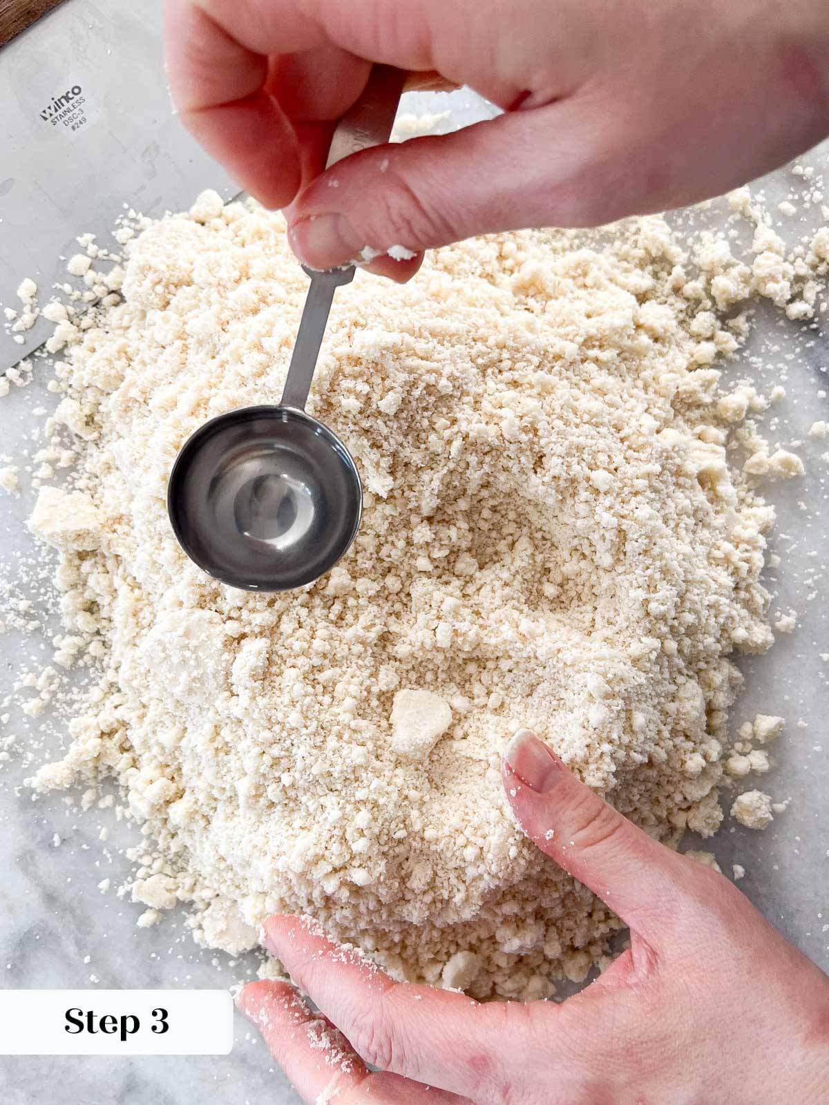 adding water by the teaspoon to pie crust dough.