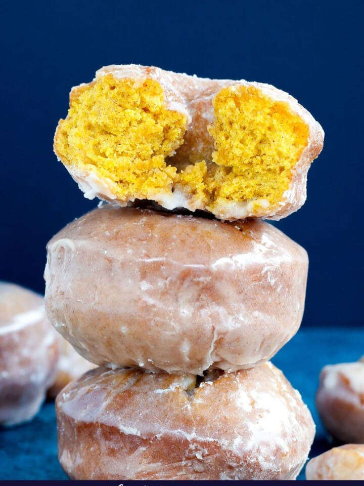 Three pumpkin donuts stacked with the top one sliced in half.