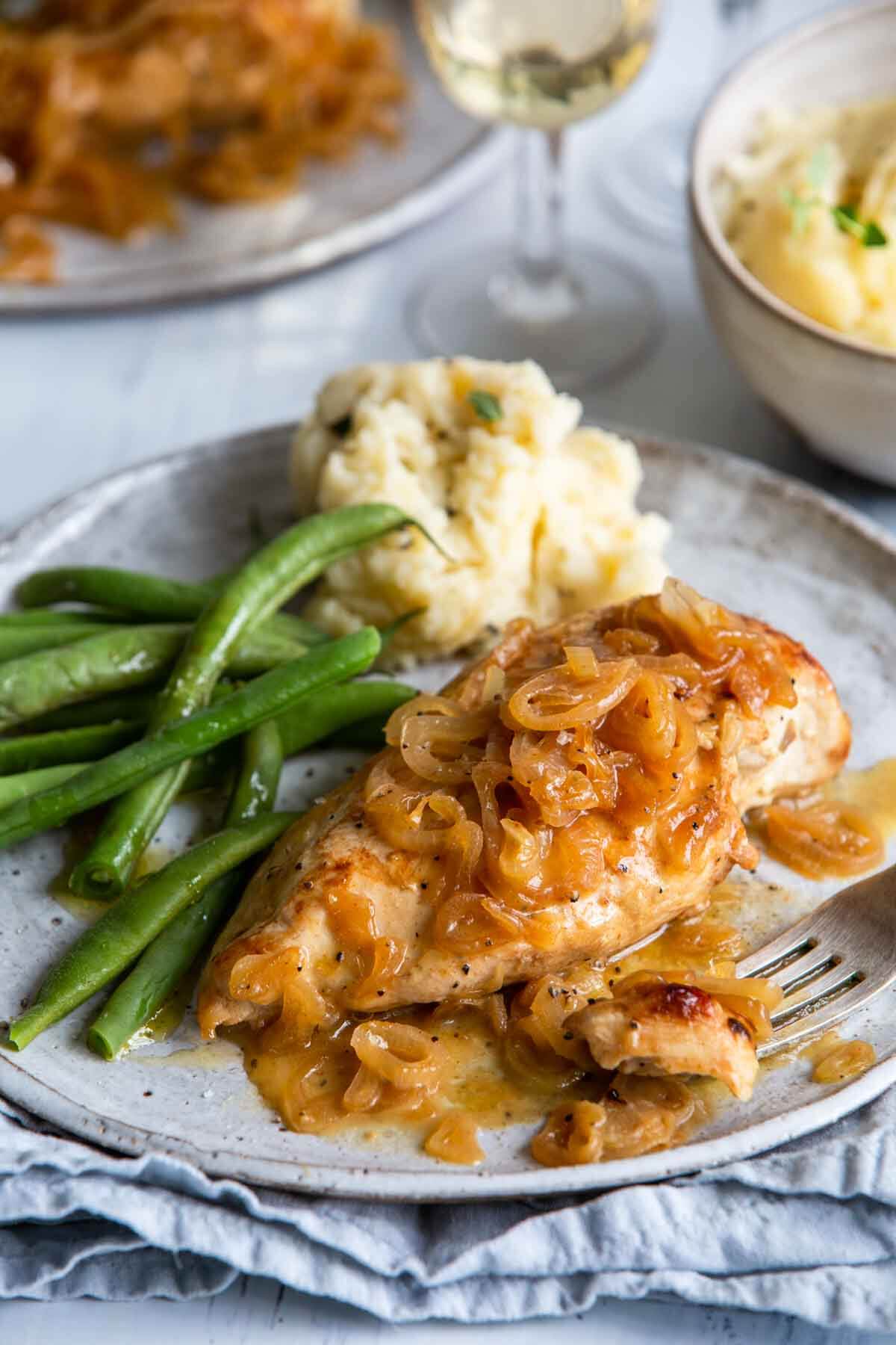Chicken with shallots on a plate with a side of green beans.