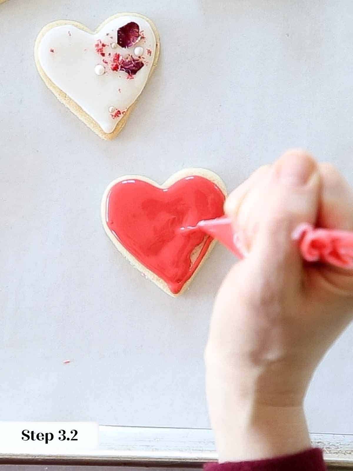 flooding red royal icing on heart shaped sugar cookie.