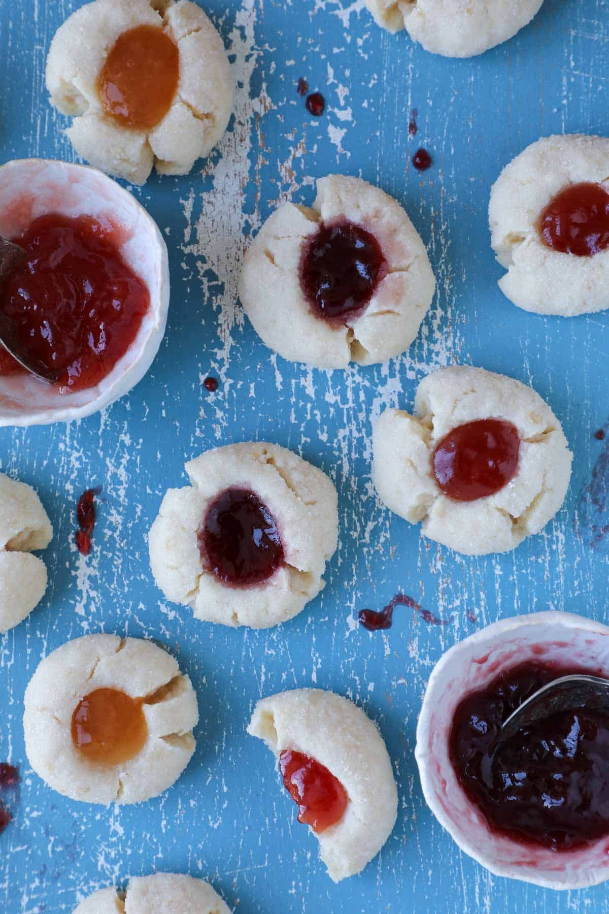 many thumbprint cookies with jam in small white bowls.