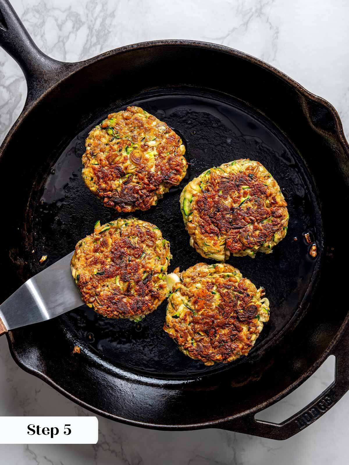 4 zucchini fritter patties cooked to golden brown in cast iron pan.
