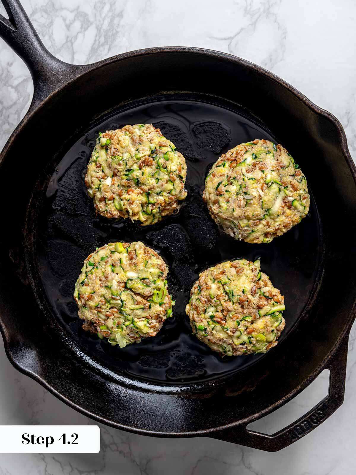 4 zucchini fritter patties uncooked in cast iron pan.