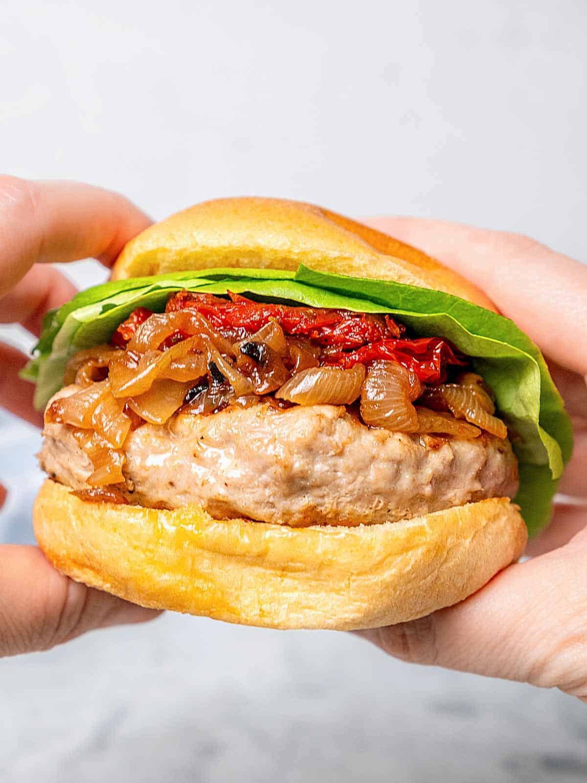 holding turkey burger with toppings and brioche bun.