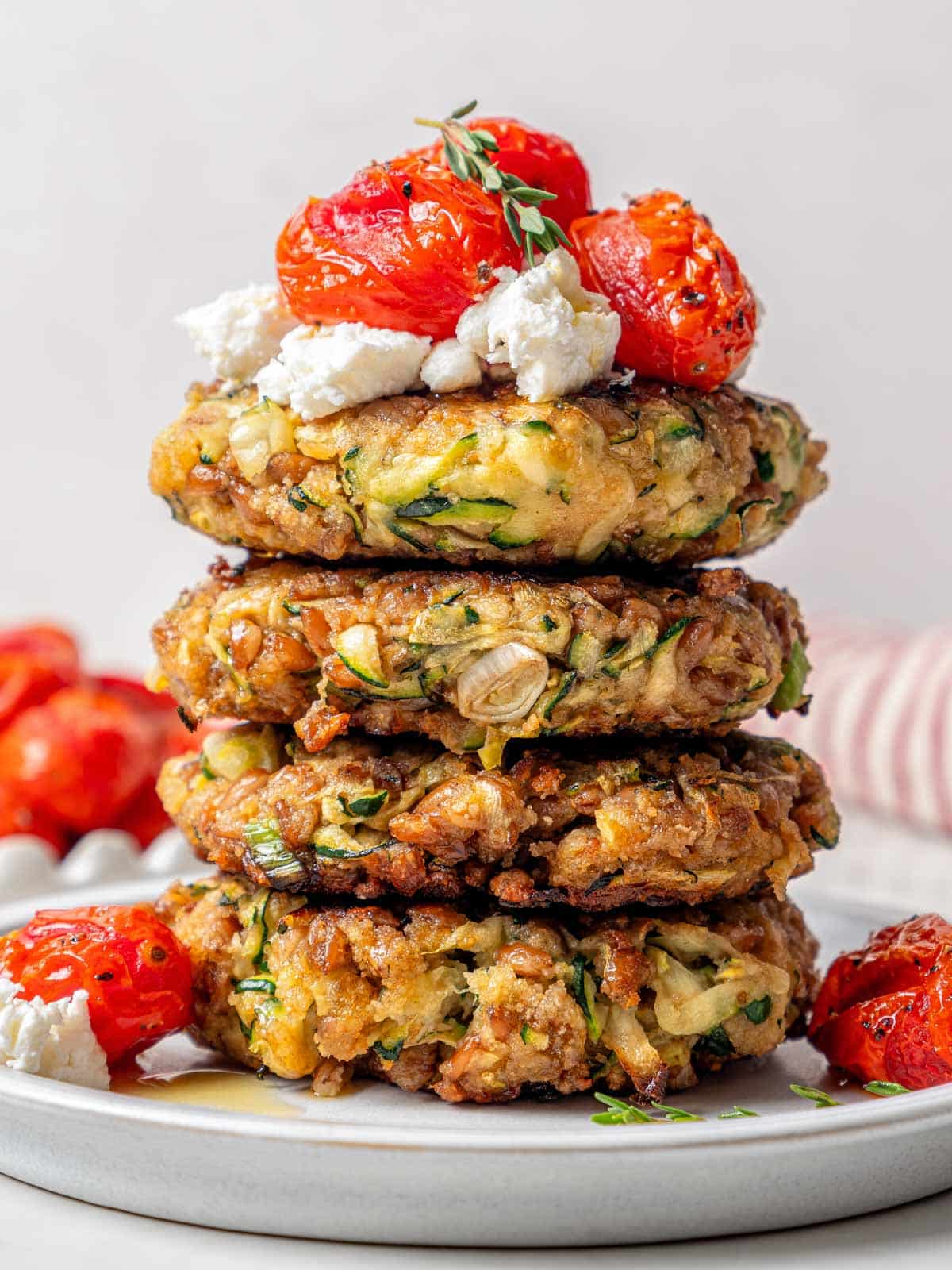 stack of 4 zucchini fritters with cheese and tomatoes. 
