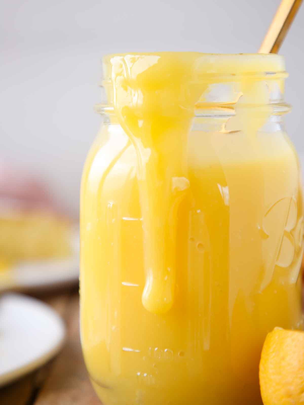 lemon curd in mason jar with cake sliced in background. 