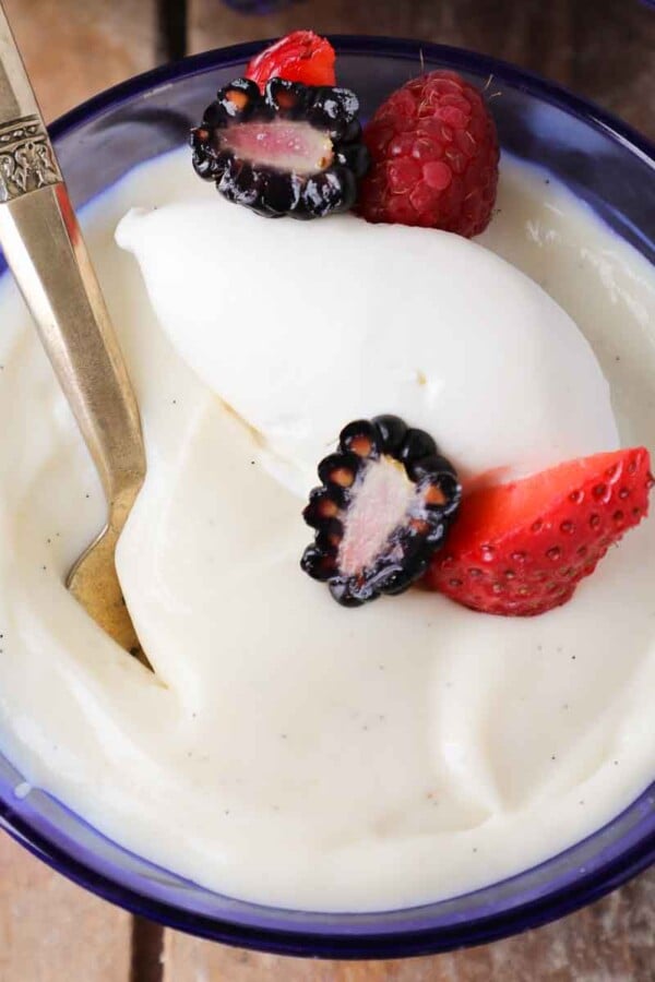 vanilla pudding with whipped cream in a blue bowl and berries.