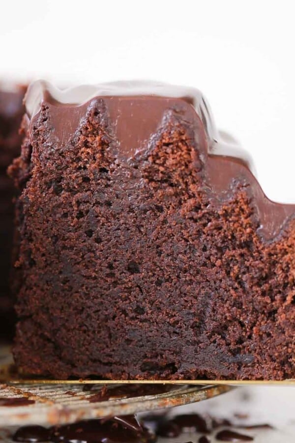 slice of chocolate bundt cake with ganache on gold cake server.