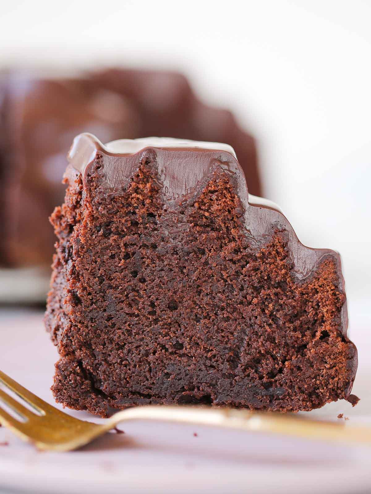 slice of chocolate bundt cake with ganache on gold cake server.