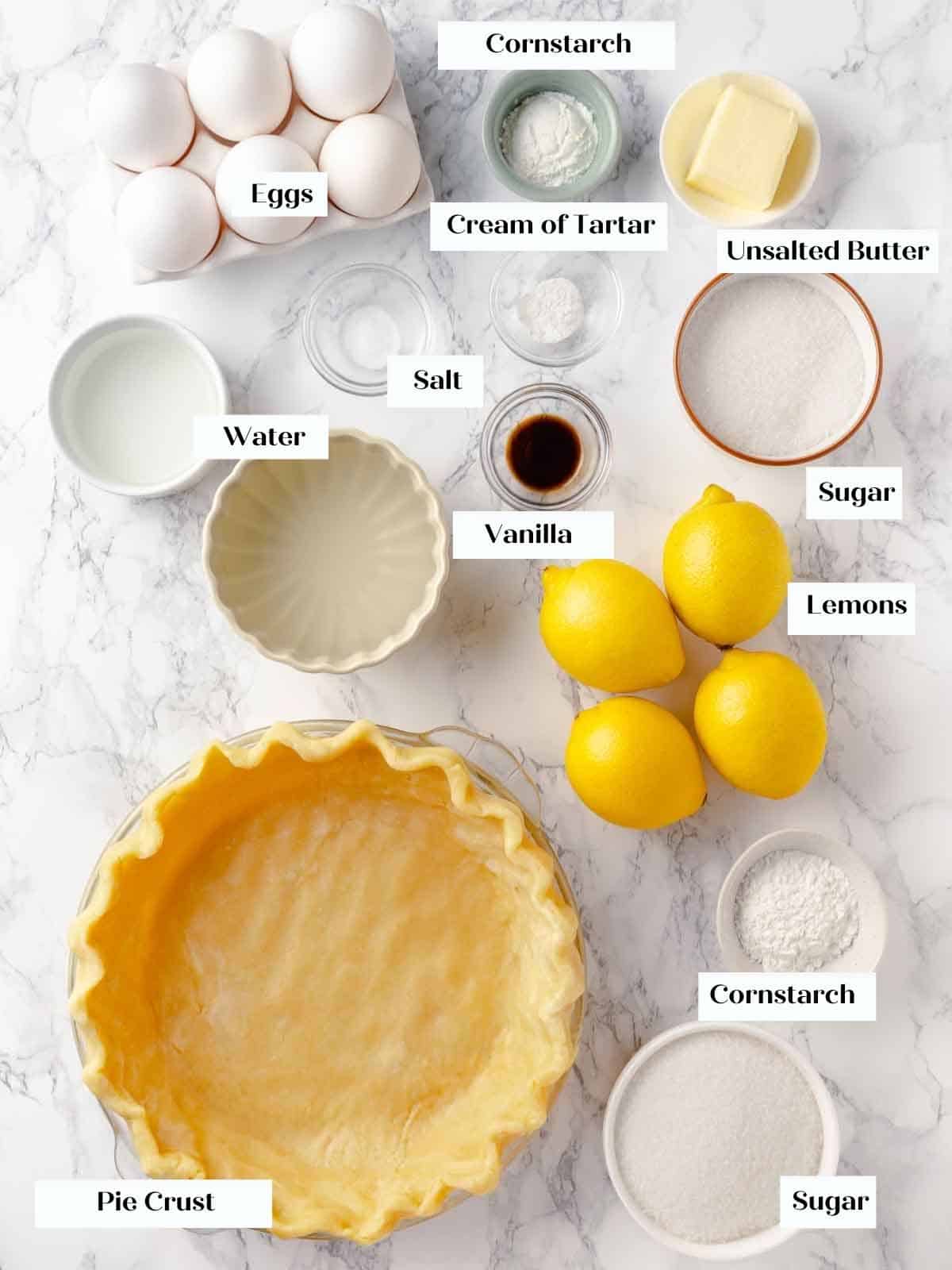 A display of ingredients on a white marble surface, ready for making lemon meringue pie.