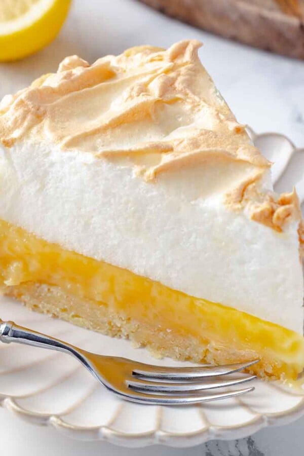 A slice of lemon meringue pie with a silver fork resting beside it, ready to be eaten.