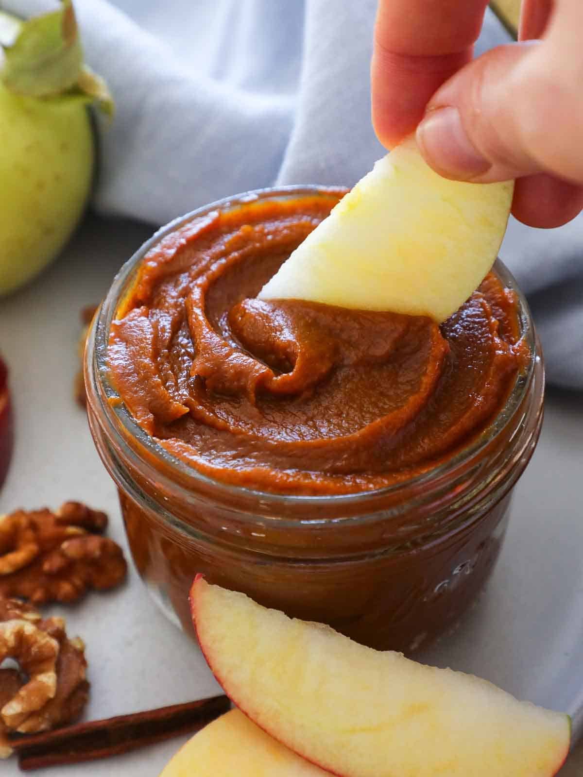 scooping pumpkin butter from jar with apple slice in hand.