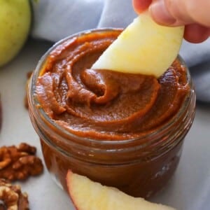 scooping pumpkin butter from jar with apple slice.