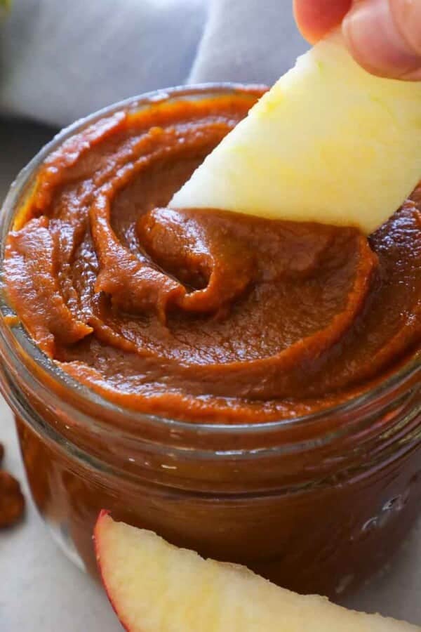 scooping pumpkin butter from jar with apple slice.