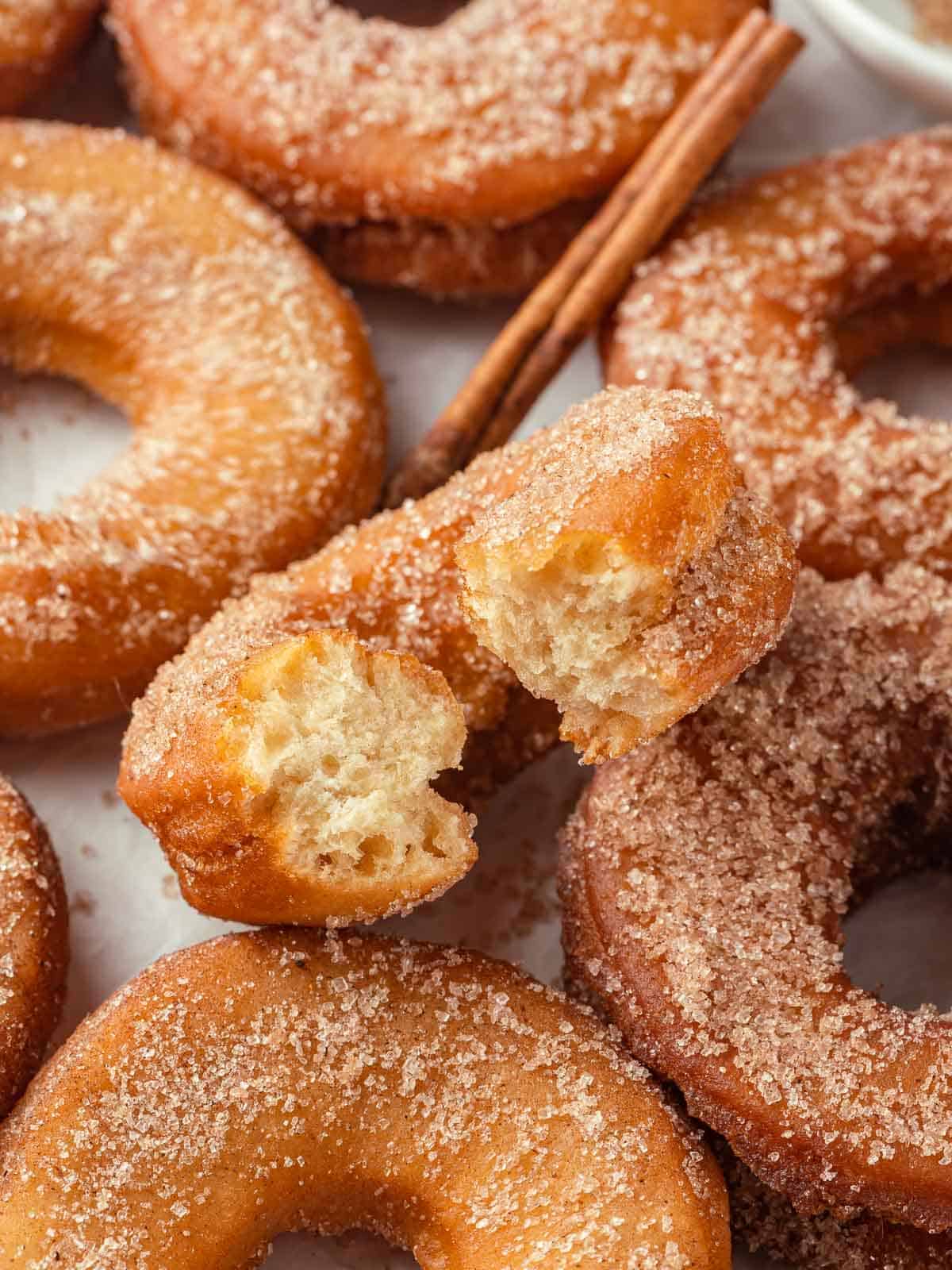 A close-up of apple cider donuts placed next to a cinnamon stick, emphasizing the cozy, autumnal flavor.