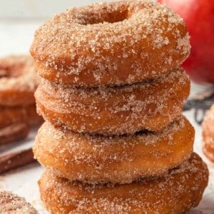 Four apple cider donuts stacked on top of each other, capturing their fluffy, sugary appearance.