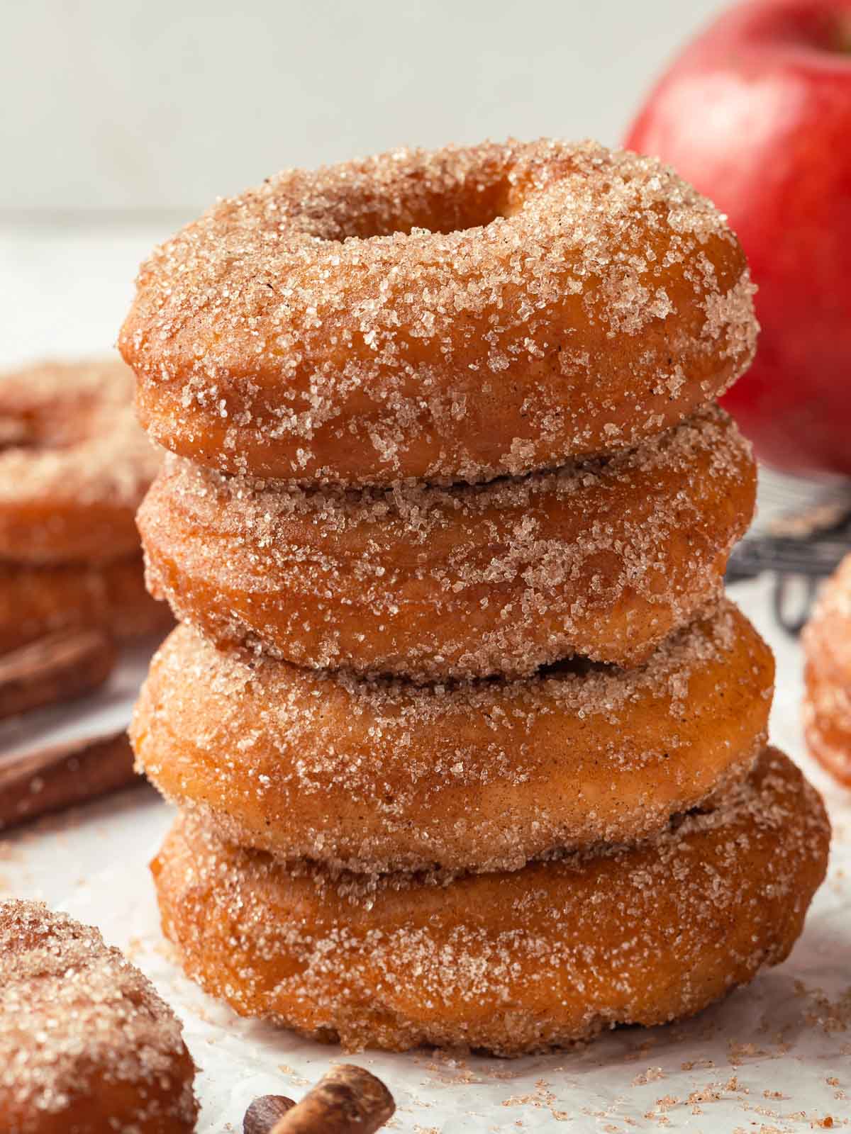 Four apple cider donuts stacked on top of each other, capturing their fluffy, sugary appearance.