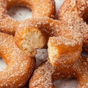 A set of apple cider donuts with the top one bitten, revealing the soft, airy interior.