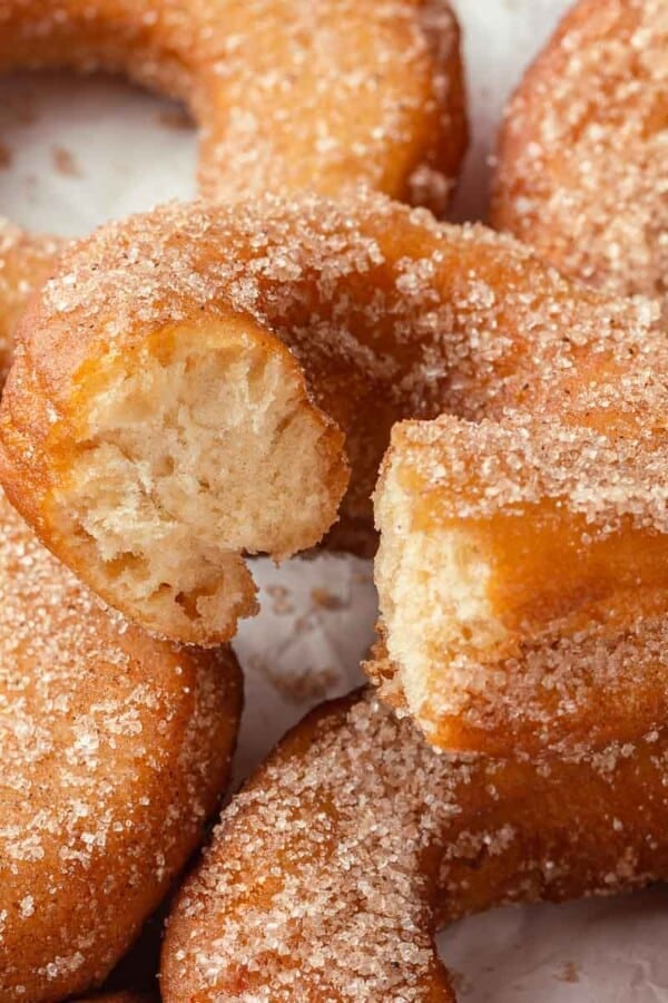 A set of apple cider donuts with the top one bitten, revealing the soft, airy interior.