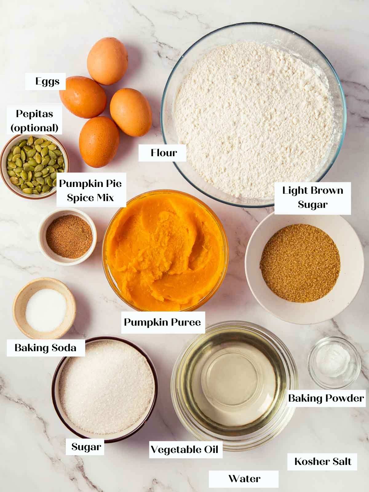 Ingredients for pumpkin bread arranged on a white marble countertop.