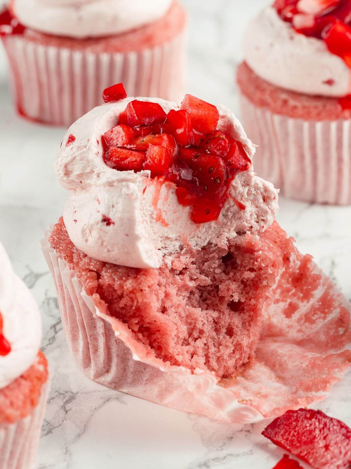 A strawberry cupcake with a bite taken out, showing the moist crumb and creamy frosting.