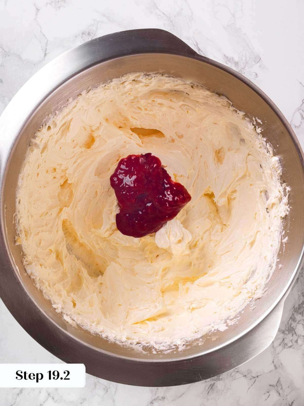 Strawberry jam being added to buttercream frosting for a rich, fruity flavor.