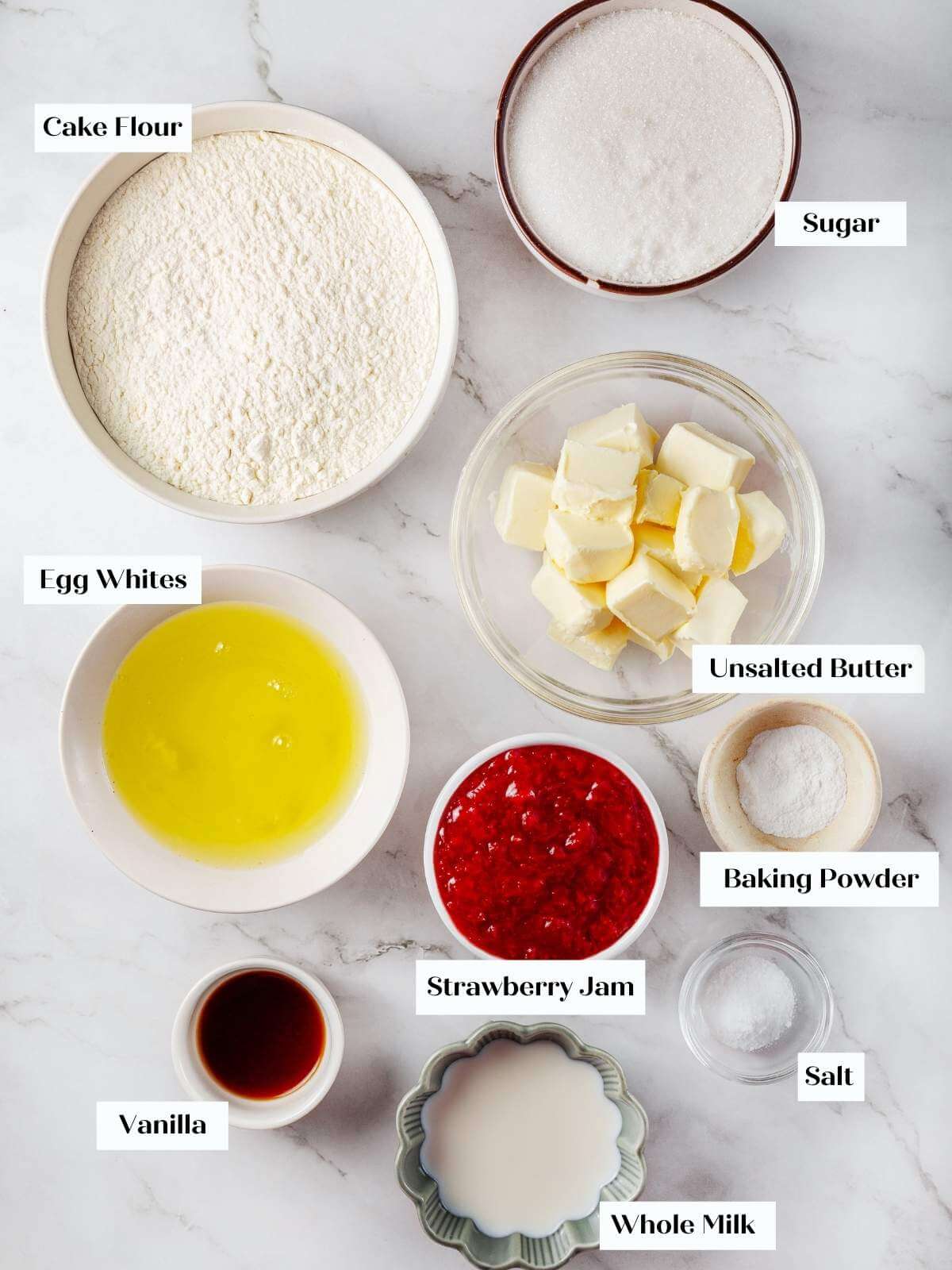 All ingredients for strawberry cupcakes, including egg whites, flour, and fresh strawberries, displayed on a countertop.