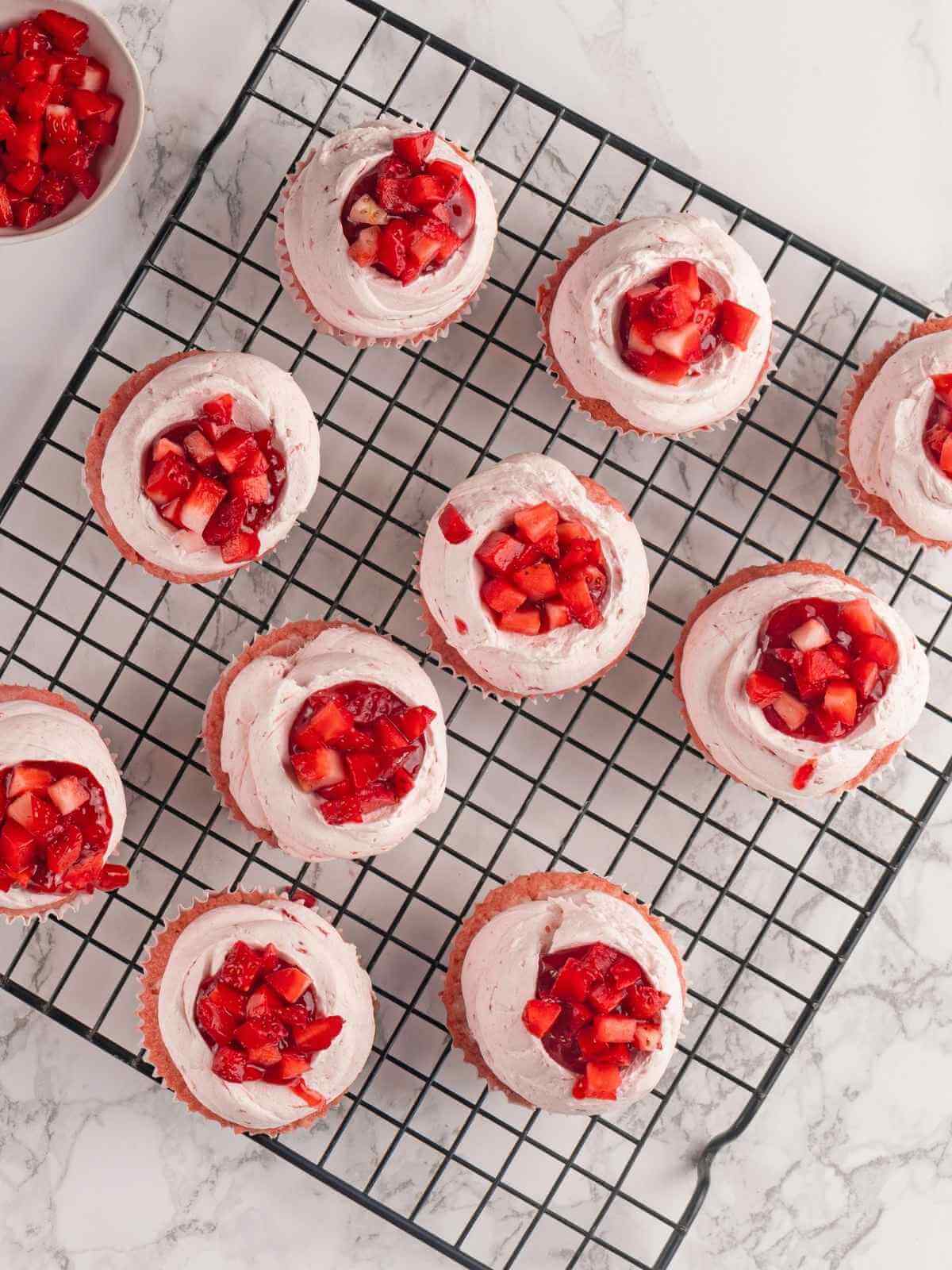 Frosted strawberry cupcakes decorated with fresh strawberries for a beautiful presentation.