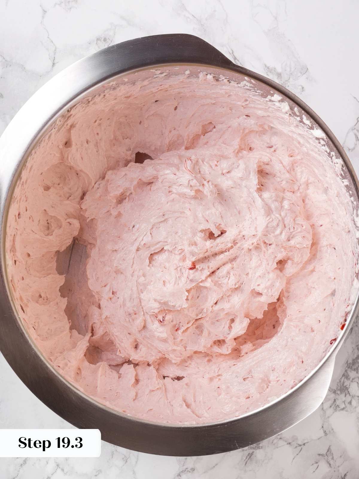 A bowl of smooth strawberry buttercream frosting ready for piping onto cupcakes.