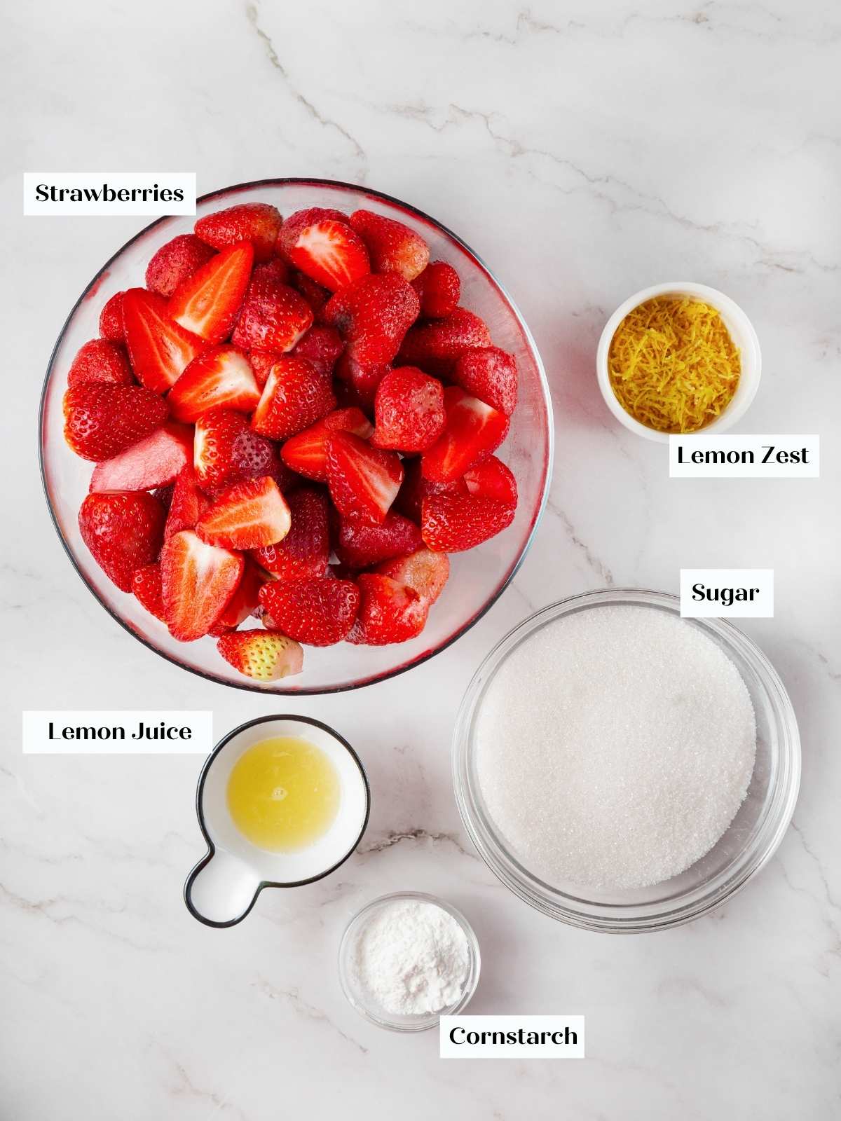 Ingredients for homemade strawberry jam, including fresh strawberries, sugar, and lemon juice, arranged on a countertop.