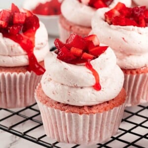 A batch of strawberry cupcakes topped with fresh strawberry and creamy buttercream.