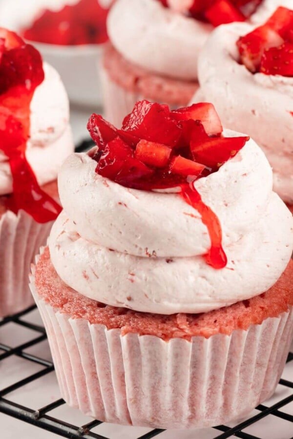 A batch of strawberry cupcakes topped with fresh strawberry and creamy buttercream.