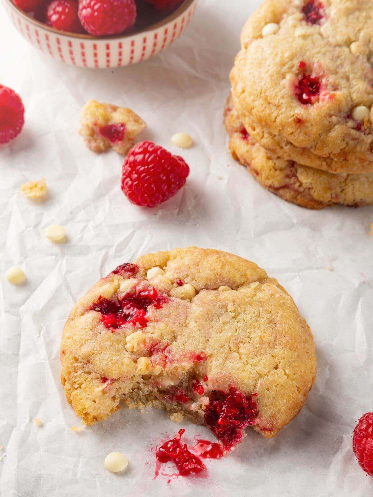 A white chocolate raspberry cookie with a bite taken out, showing its moist, flavorful texture.