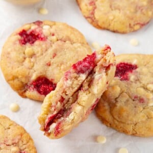 A white chocolate raspberry cookie broken in half, showing its chewy texture and gooey chocolate chips.