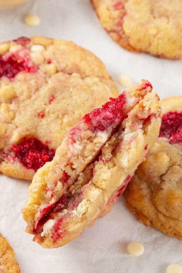 A white chocolate raspberry cookie broken in half, showing its chewy texture and gooey chocolate chips.