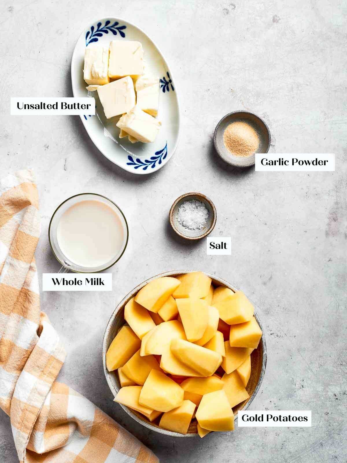 Ingredients for mashed potatoes prepped and ready, featuring gold potatoes, butter, salt, and milk in small bowls.