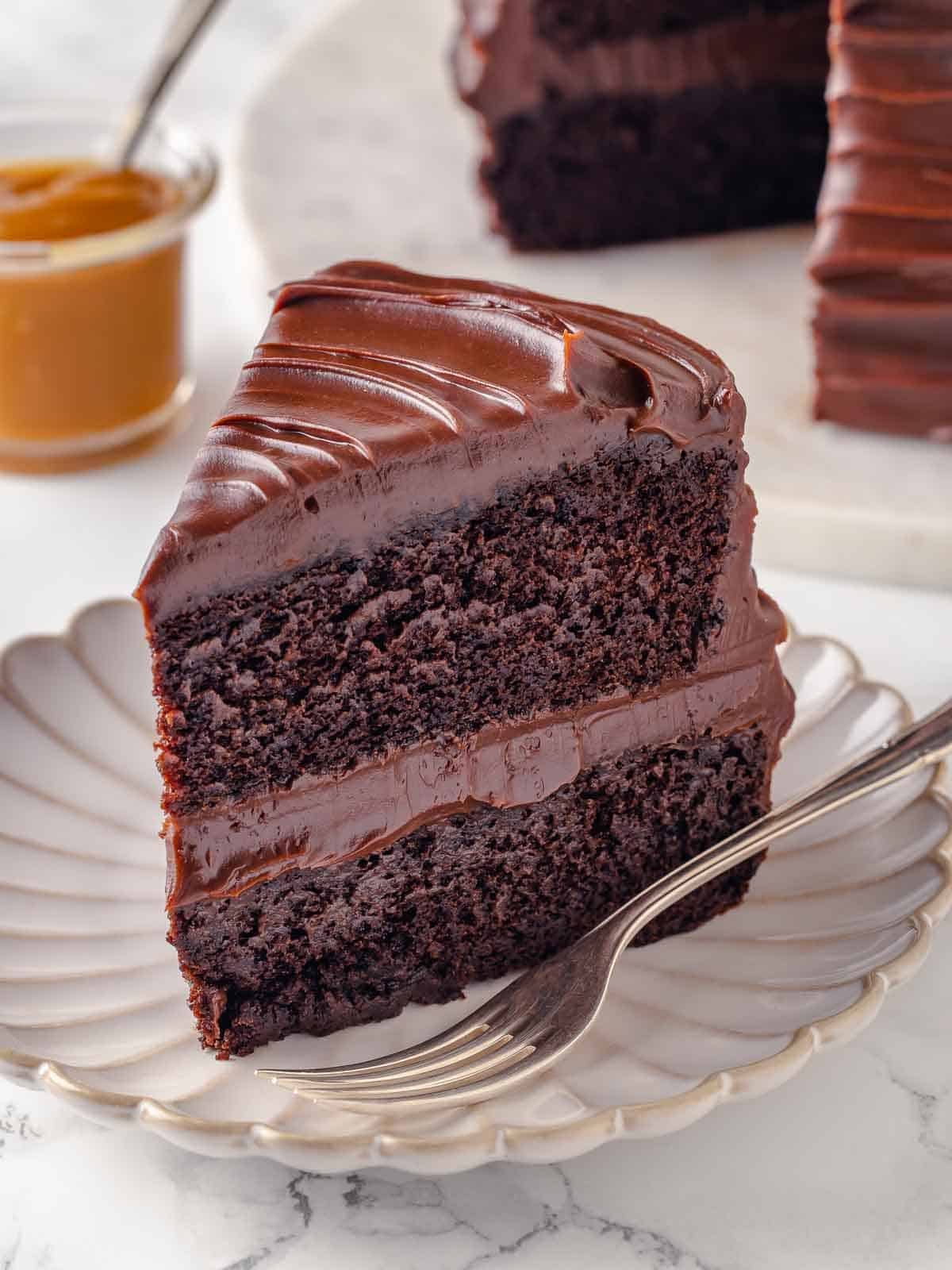 two layer guinness chocolate cake with caramel fudge frosting on scalloped plate with fork.